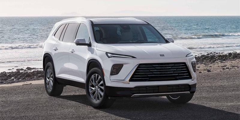 A New White 2026 Buick Enclave sitting on the pavement beside a beach with the waves rolling in behind it
