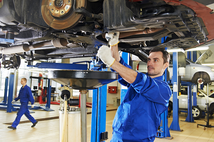White-gloved expert maintenance technician working with a tool to repair a car lifted above his head in the GMC shop